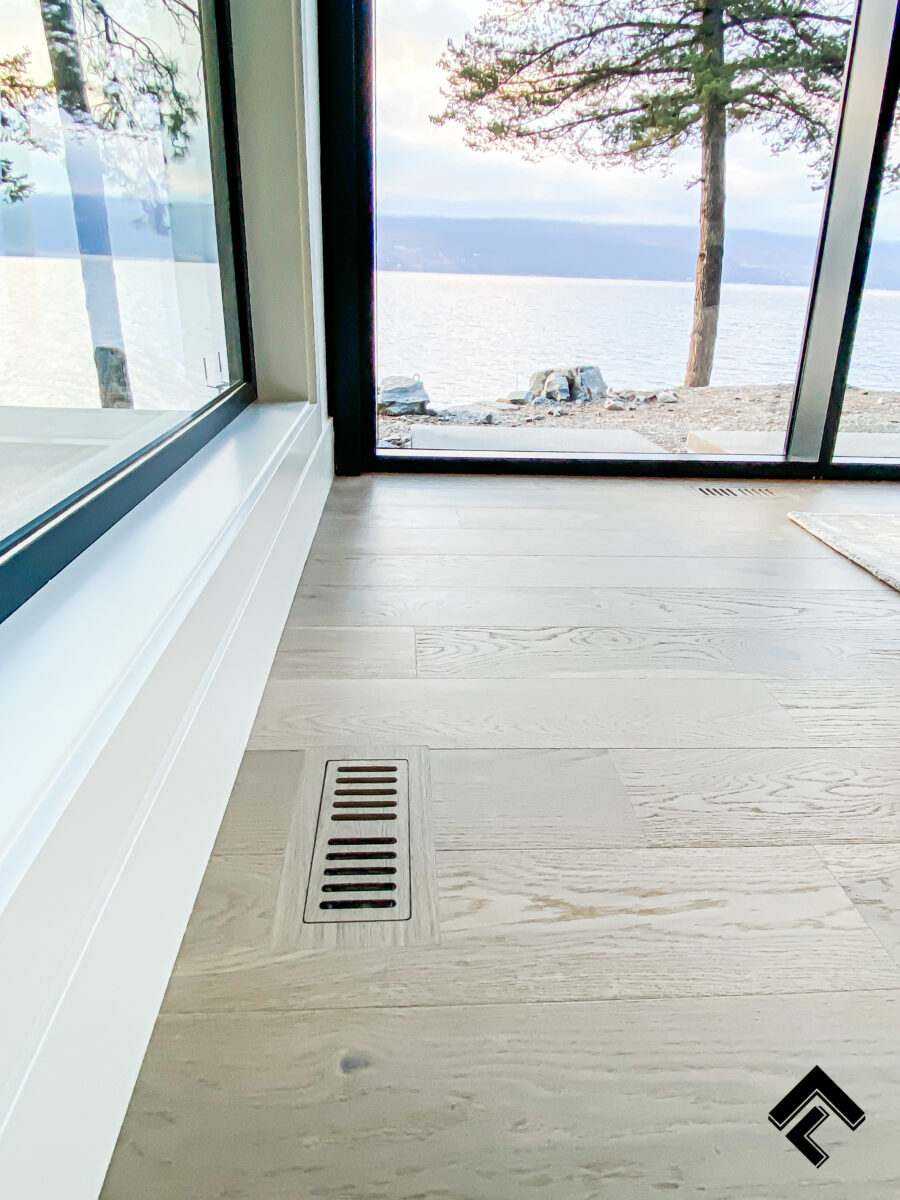 Hardwood flush framed floor vent installed in light oak flooring inside a modern lakefront home in Lake Country with scenic lake views